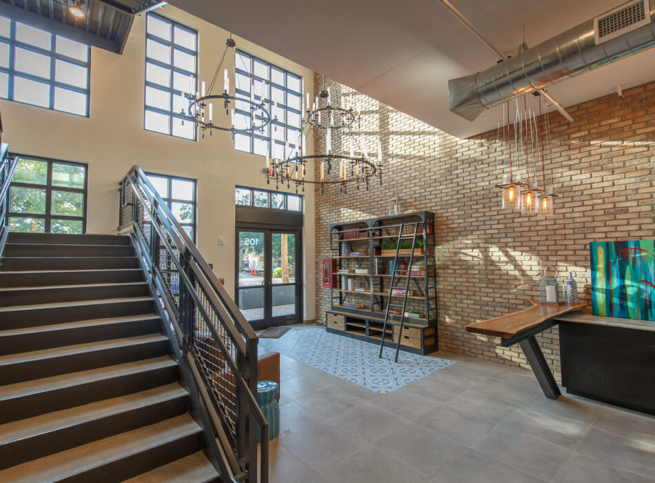 Modern lobby with brick walls, metal stairs, chandeliers, art.
