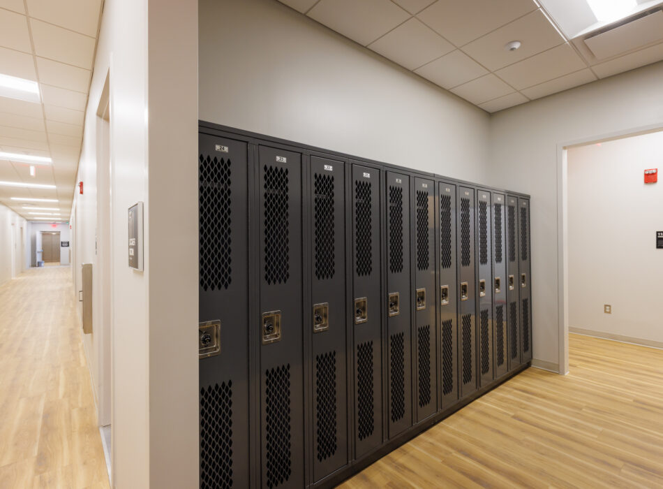 Black lockers along white wall in empty, clean hallway.