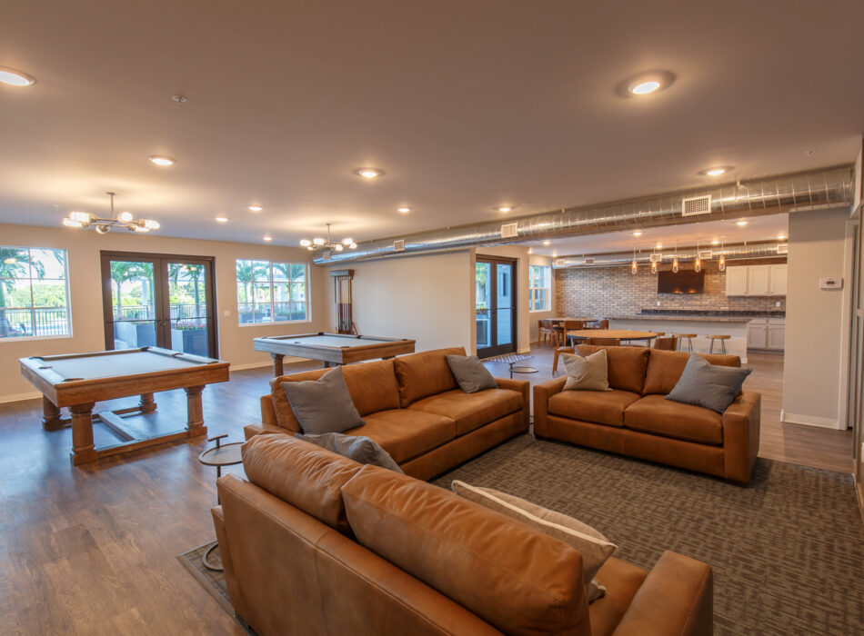 Game room with sofas, pool table, kitchen, and big windows.