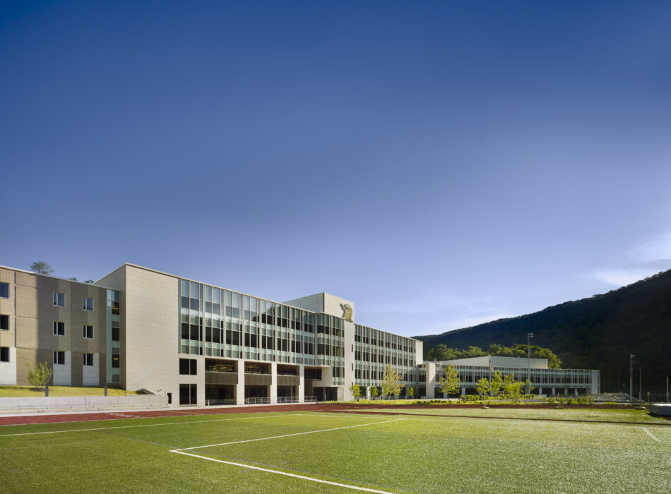 Modern school by sports field, hill and blue sky.