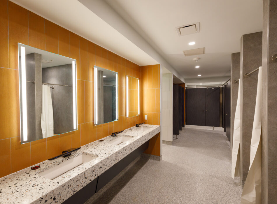 Modern restroom with terrazzo sink, mirrors, orange-gray walls, stalls.
