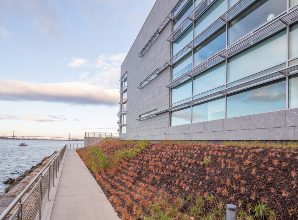 Modern building with large windows beside water and walkway.