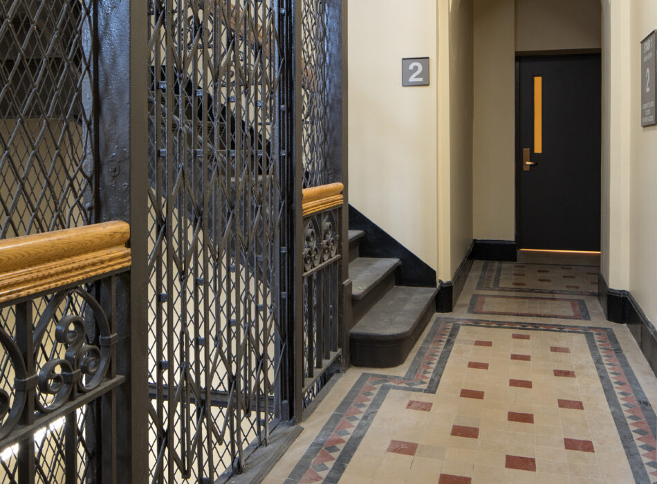 Tiled hallway with gated elevator, stairs, and black door.