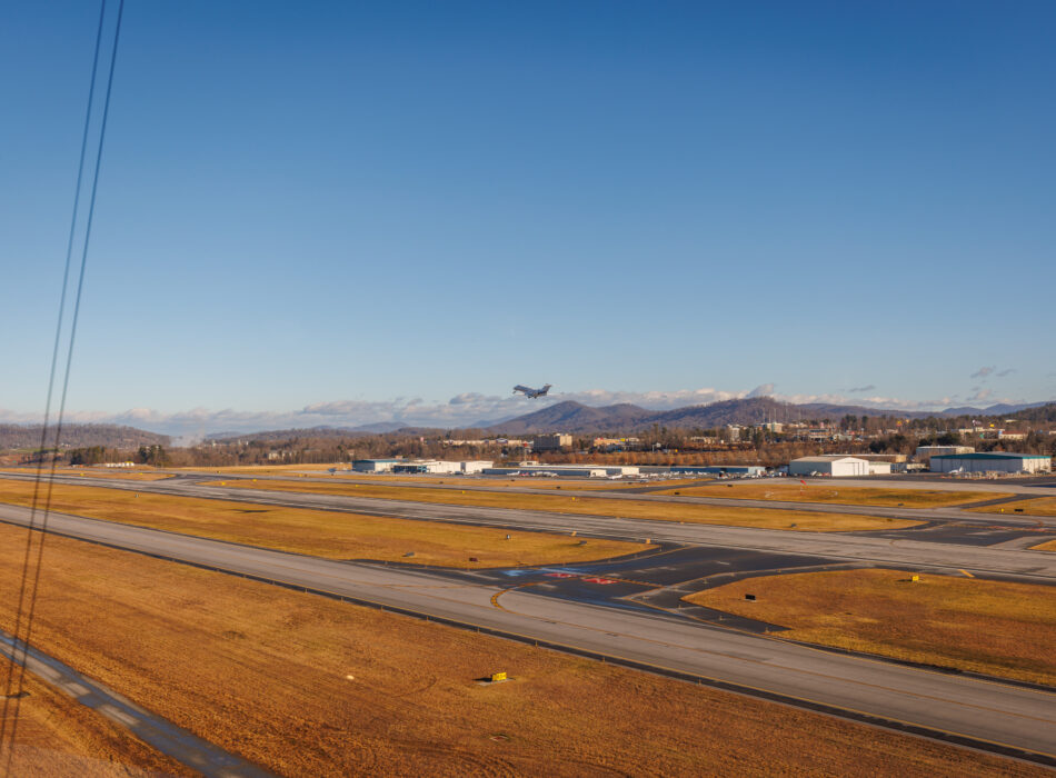 Jet takes off from runway with mountains in background.