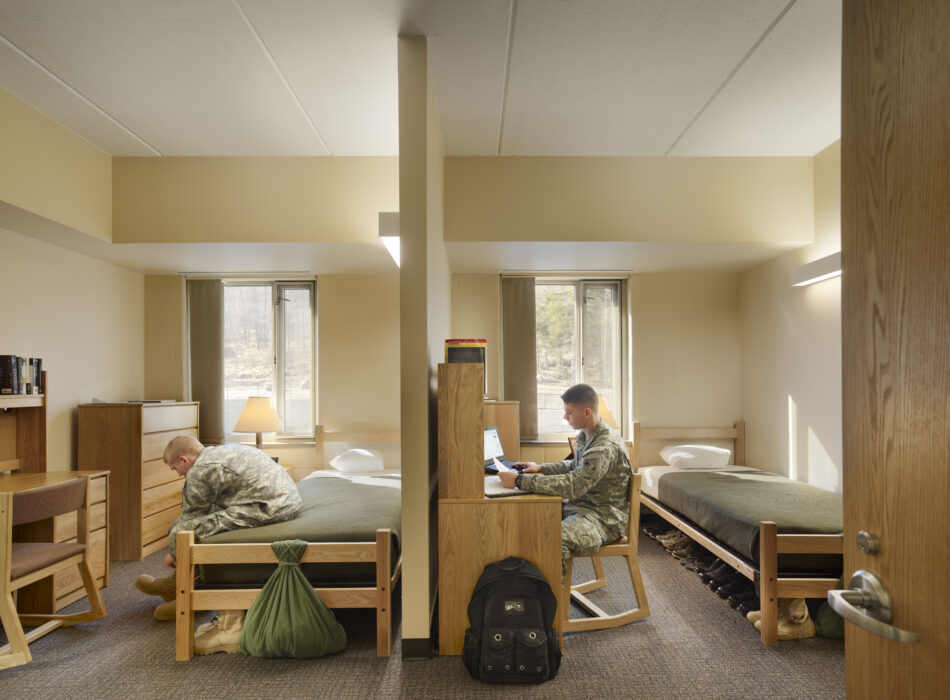 Two uniformed people in a divided dorm room, working separately.