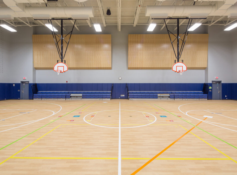 Empty gym with wooden floor, hoops, benches, and markings.