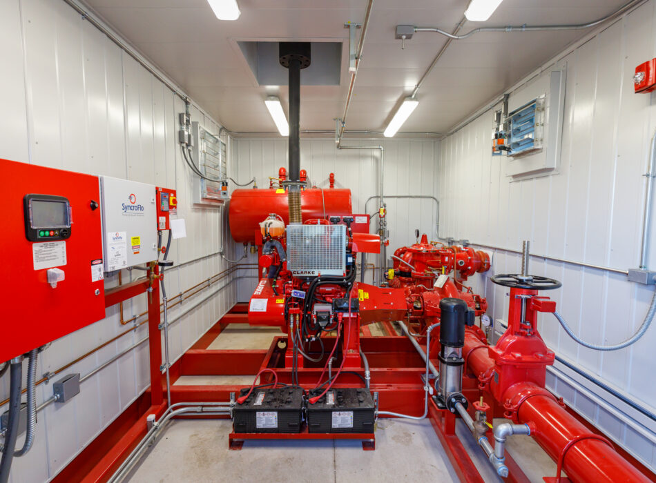 Red fire pump system with pipes in white mechanical room.