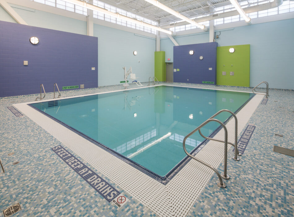 Empty indoor pool, blue-green walls, railings, tiled floor.