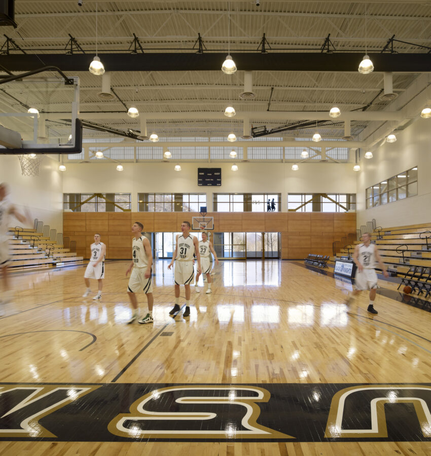 Seven basketball players practice in a bright gym.