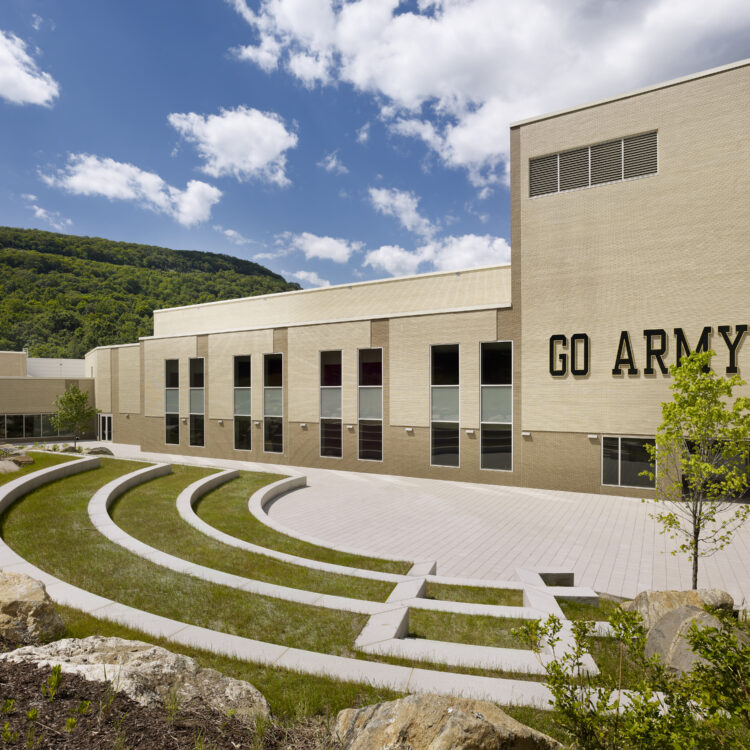 Beige GO ARMY building by seating, rocks, trees, blue sky.
