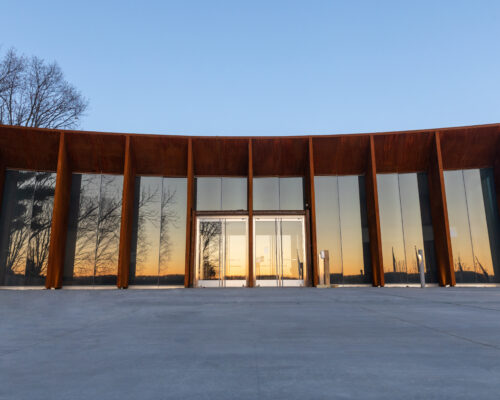 Modern glass building reflecting trees and sunset, clear sky.