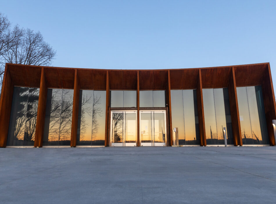 Modern glass building reflecting trees and sunset, clear sky.