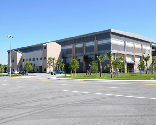 Modern building, parking lot, landscaped greenery, clear blue sky.