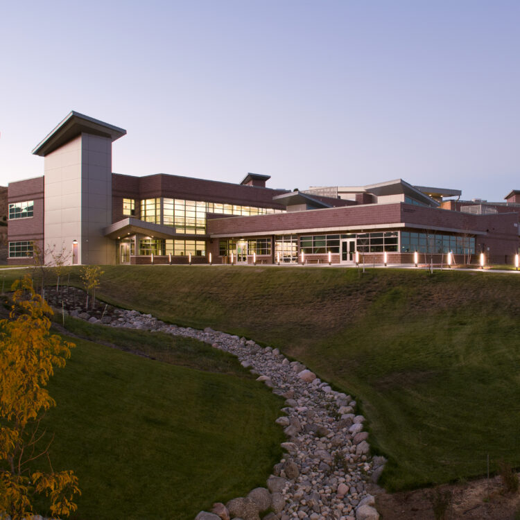 Modern building with large windows on grassy dusk landscape.