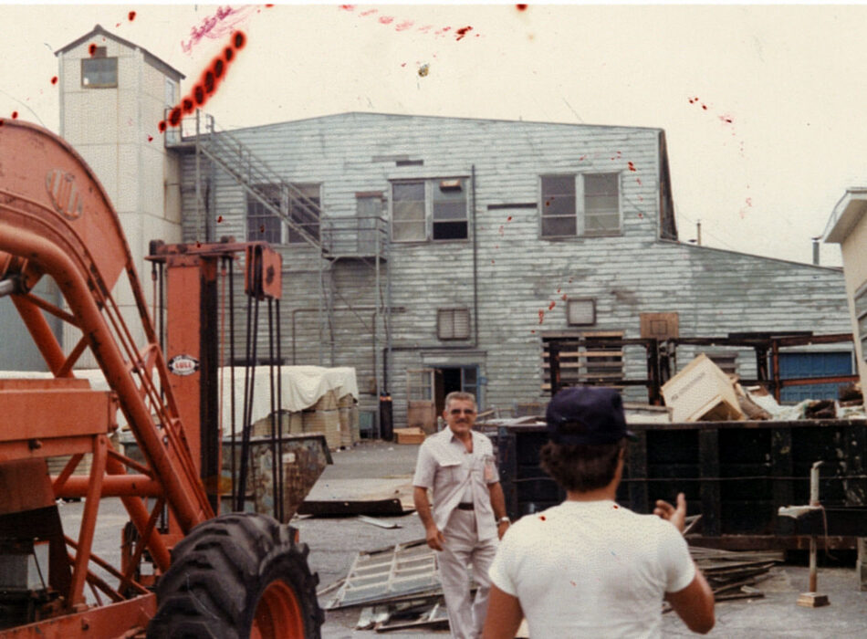 Two men in industrial yard; one faces camera, one turned.