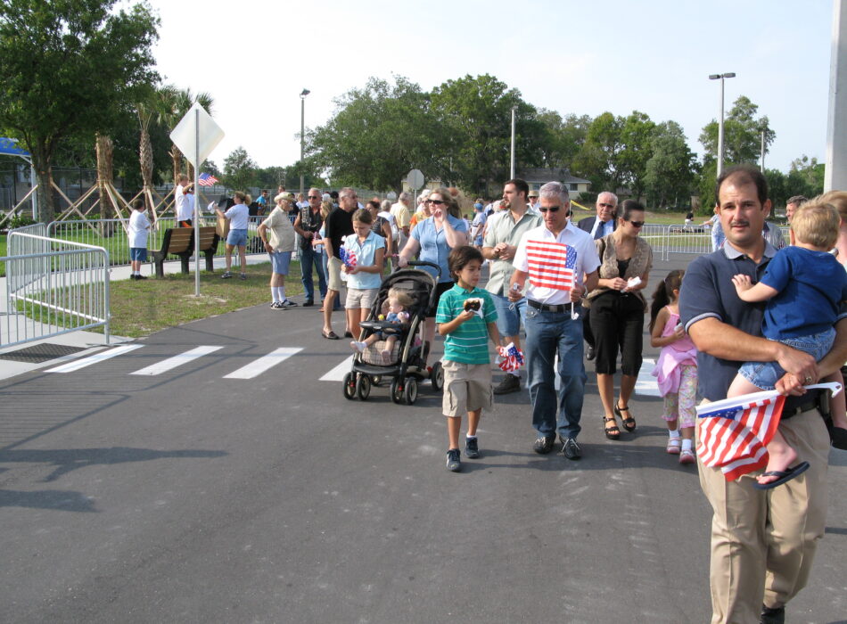Families with flags walk on a path outdoors.