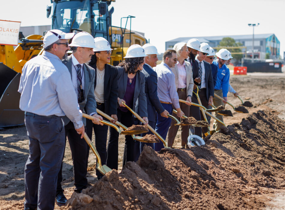 People in hard hats break ground with shovels.