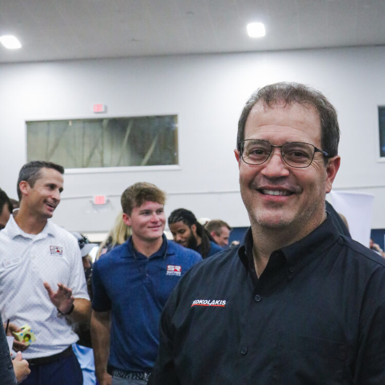 Man in black shirt smiles at indoor event.