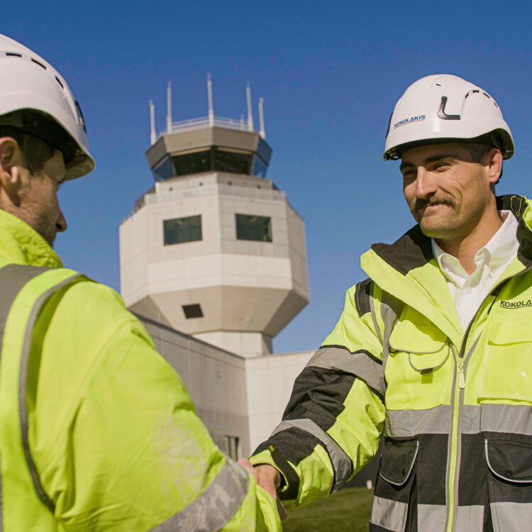 Workers in safety gear shake hands by control tower.