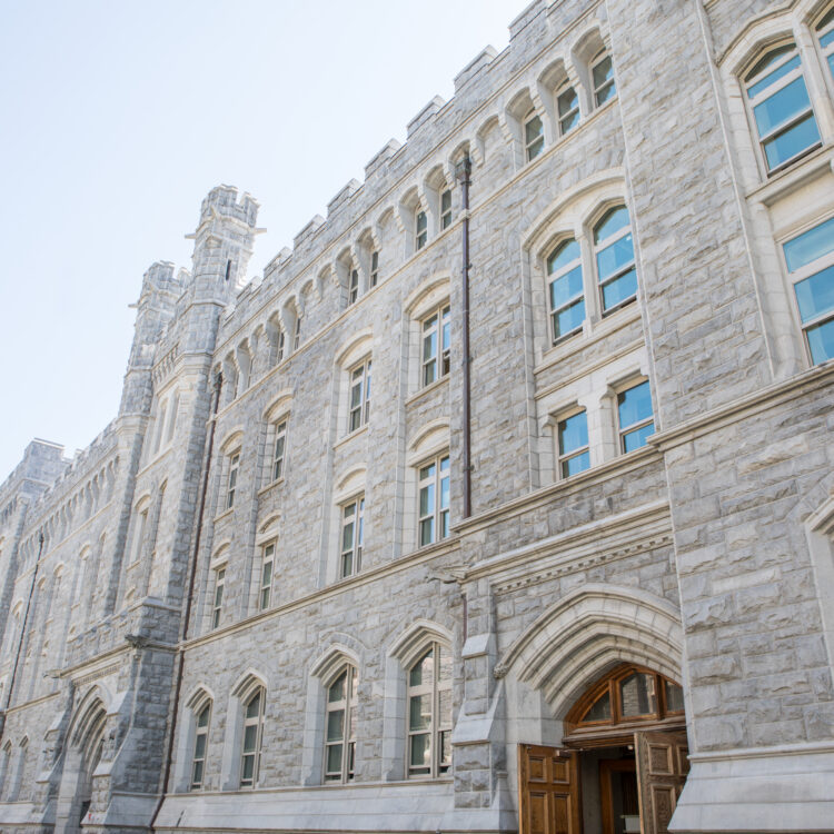 Stone building, arched windows, wooden doors, clear sky.